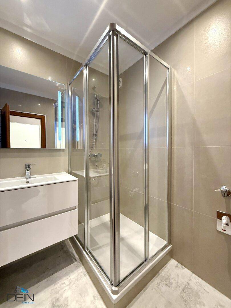 Modernes Badezimmer mit Duschkabine, Einzelwaschbecken und beigefarbenen Wandfliesen.