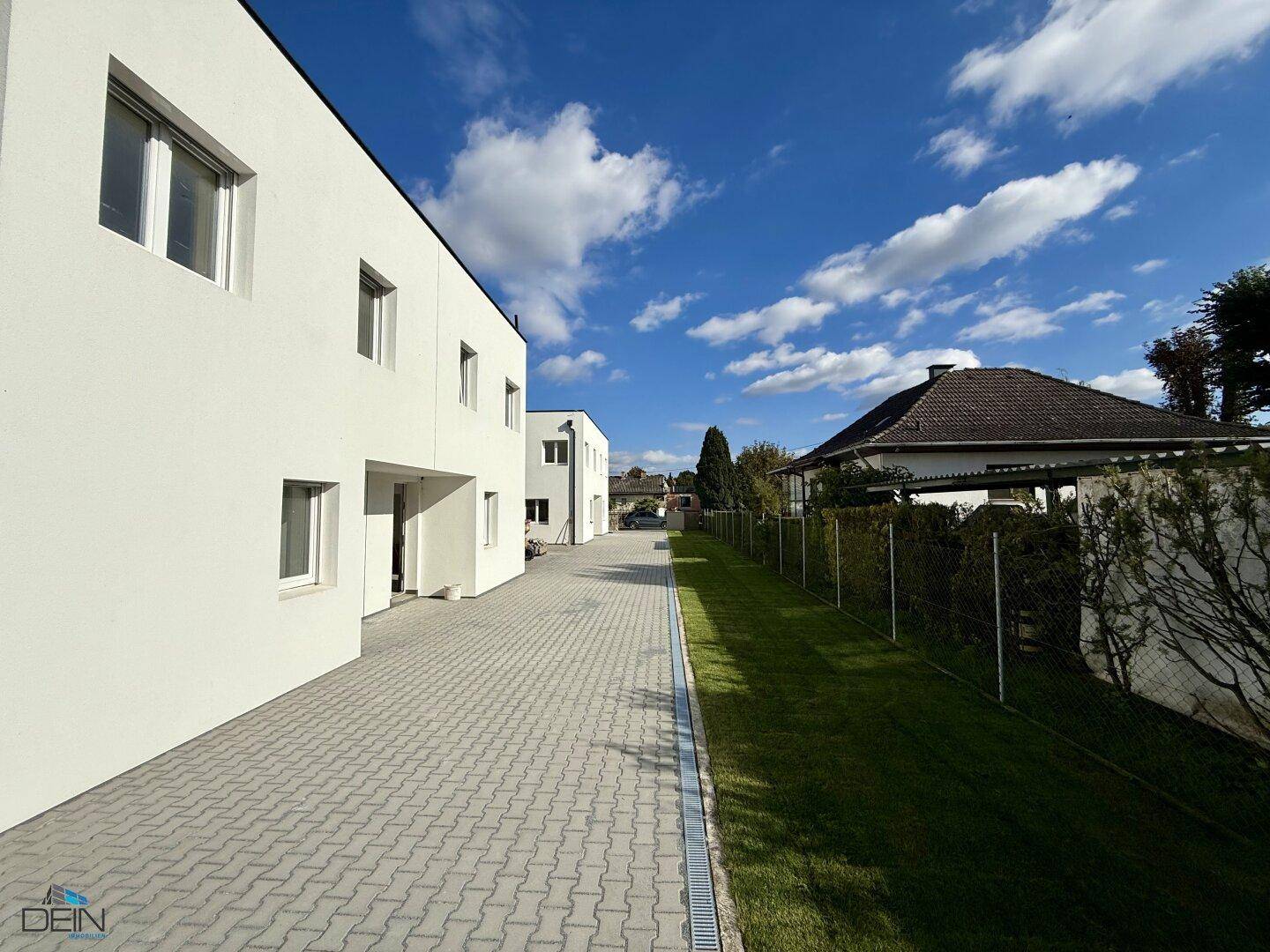 Seitenansicht der Neubauten mit gepflastertem Zugang und angrenzendem gepflegten Grünbereich.