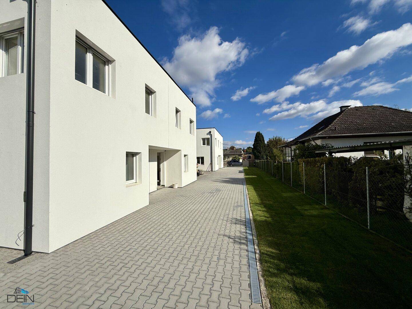 Moderne Neubauten mit sauberem Zufahrtsweg und gepflegtem Grünstreifen unter blauem Himmel.