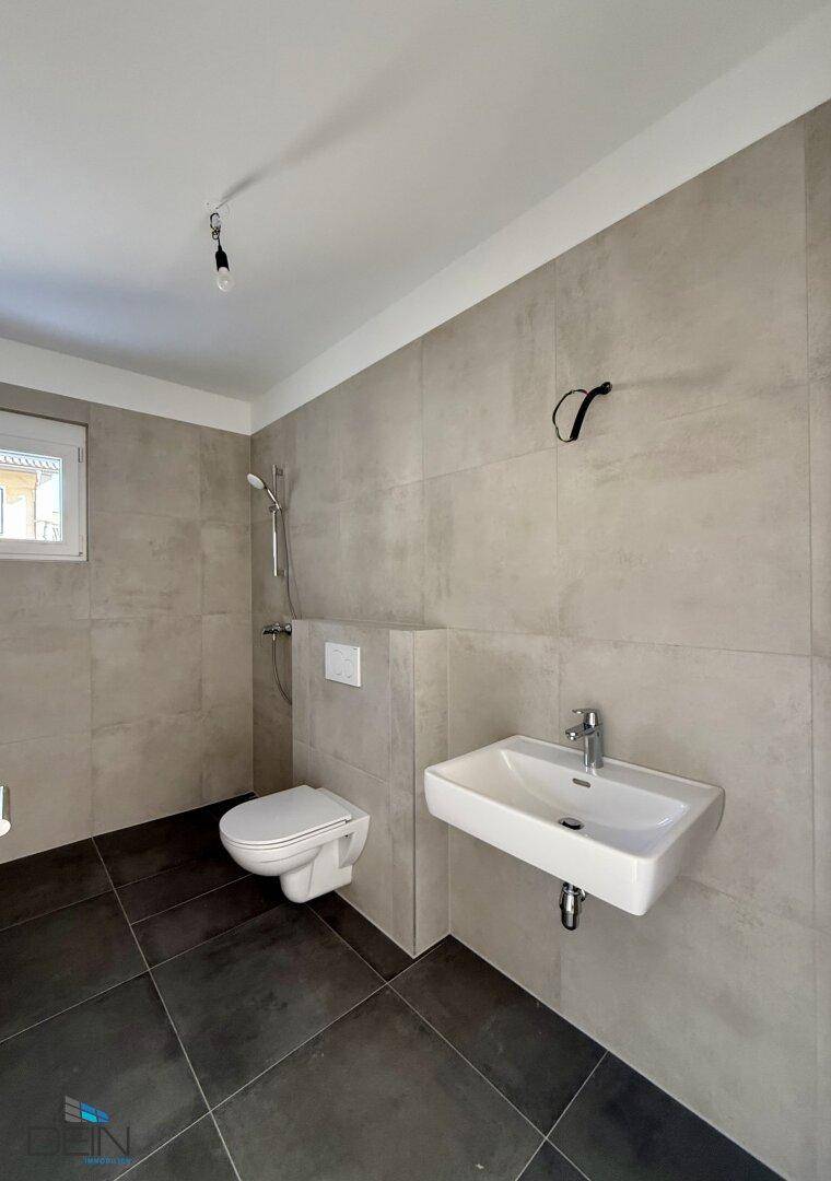 Zeitgemäßes Badezimmer mit grauen Fliesen, Duschanschluss und modernem Waschtisch.