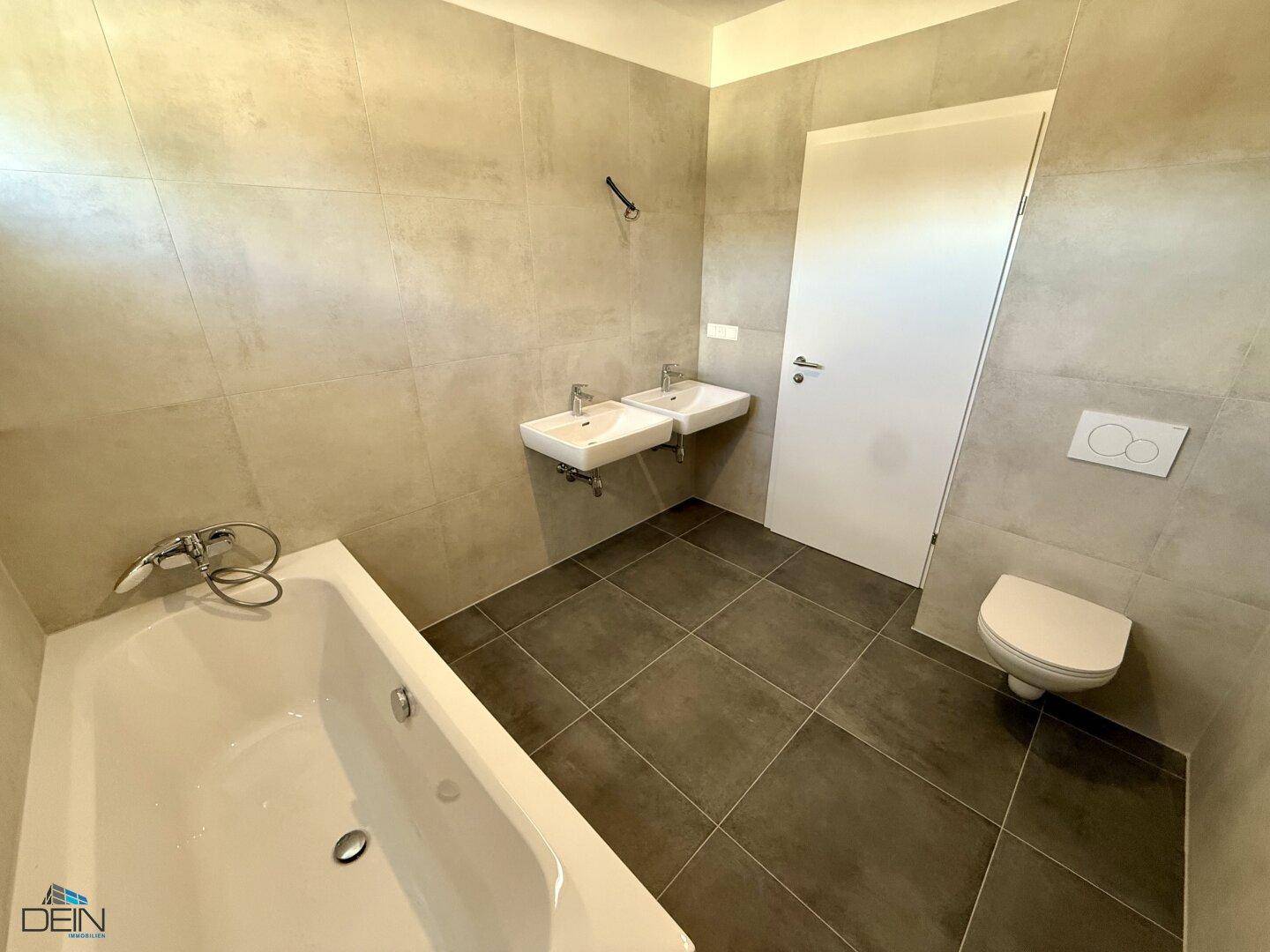 Geräumiges Badezimmer mit Badewanne, Doppelwaschbecken und wandhängendem WC.