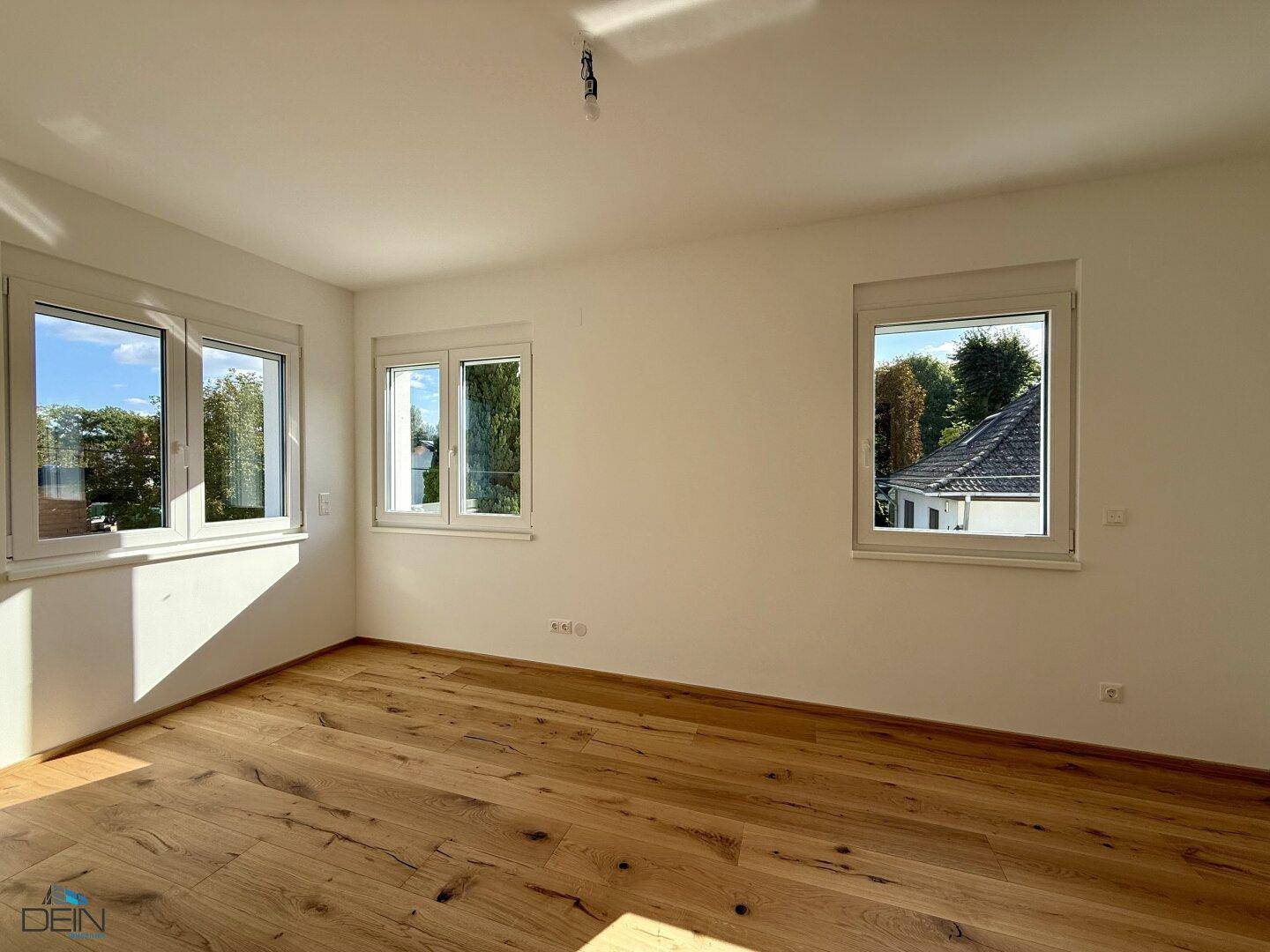 Helles Schlafzimmer mit Holzboden und mehreren Fenstern mit Blick ins Grüne.