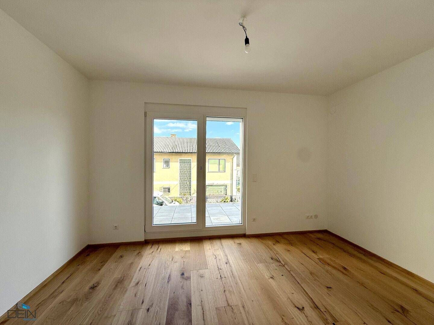 Geräumiges Schlafzimmer mit Holzboden und großem Fenster mit Zugang zur Außenterrasse.