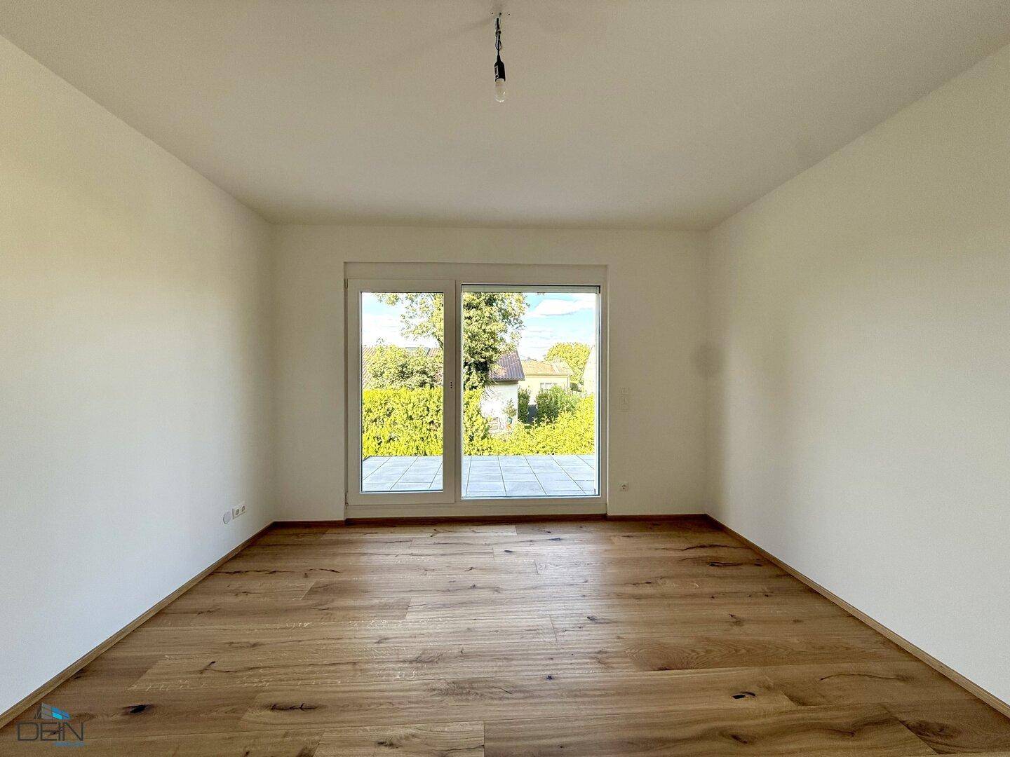 Helles Zimmer mit Holzboden und großem Fenster mit Blick ins Grüne.
