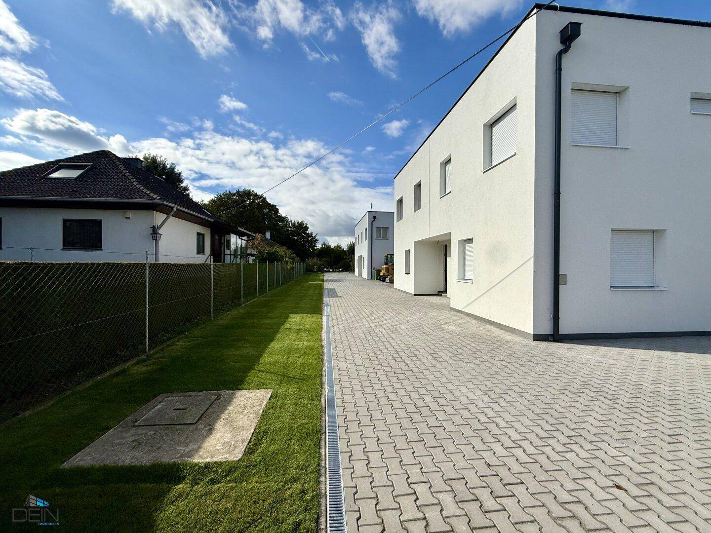Seitenansicht der modernen Gebäude mit gepflasterter Zufahrt und einem gepflegten Grünstreifen.