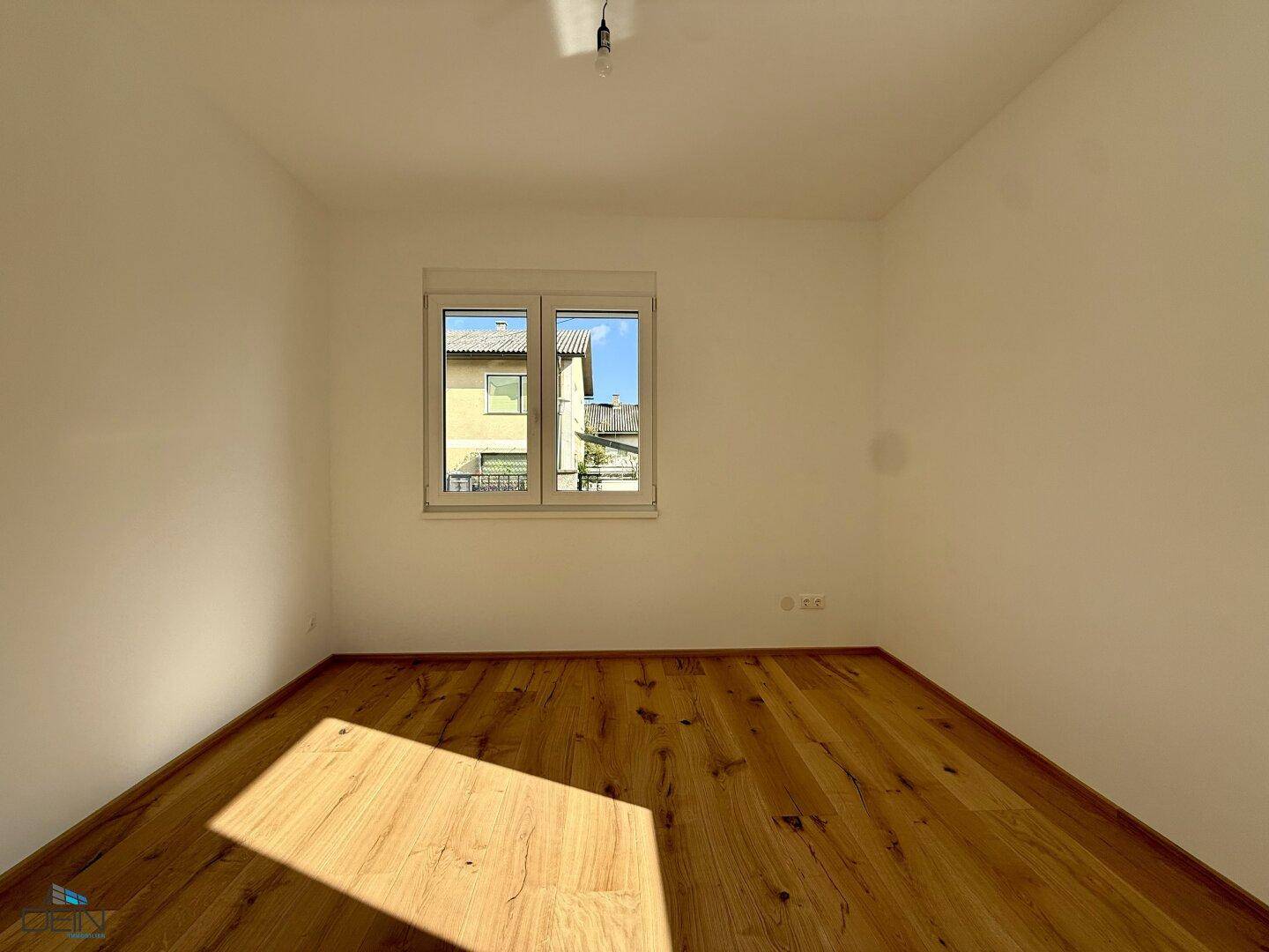 Unmöbliertes Schlafzimmer mit Holzboden und einem Fenster, das den Raum mit natürlichem Licht erhellt.