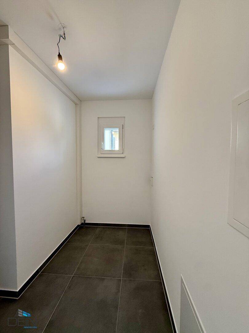 Kleiner Hauswirtschaftsraum oder Abstellraum mit Fenster und dunklem Fliesenboden, ideal für zusätzlichen Stauraum.