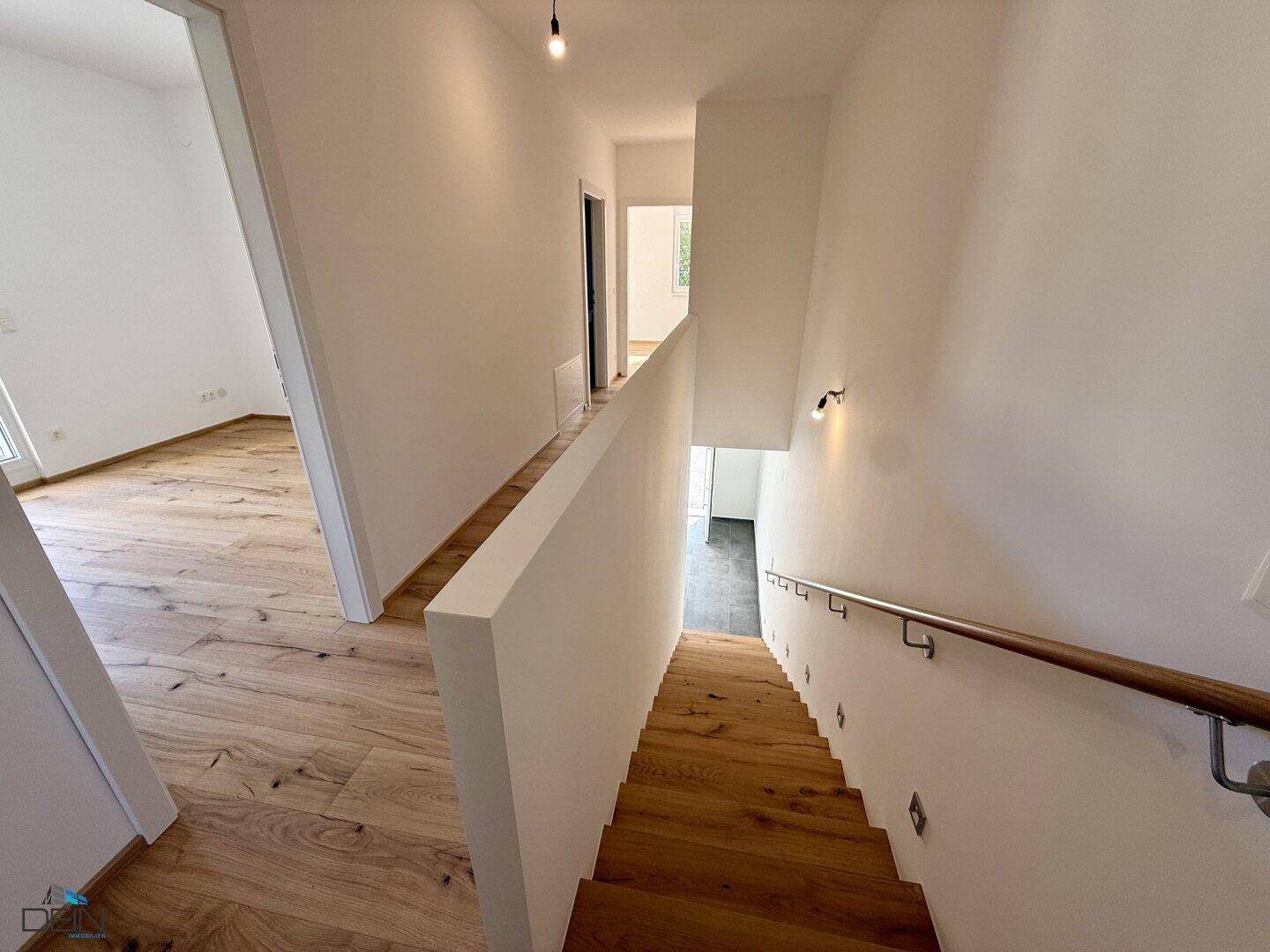 Heller Treppenaufgang mit Holzstufen und weißer Brüstung, der elegant in die obere Etage führt.