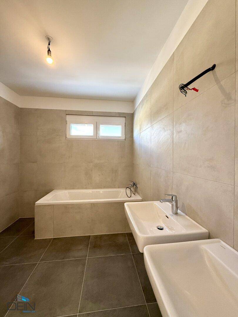 Modernes Badezimmer mit Badewanne, Doppelwaschbecken und Fenster, in neutralen Farben gefliest.