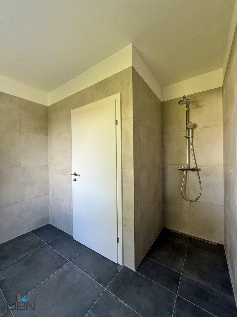 Modernes Badezimmer mit Duschbereich und dunklem Fliesenboden, in neutralen Farben gehalten und pflegeleicht.