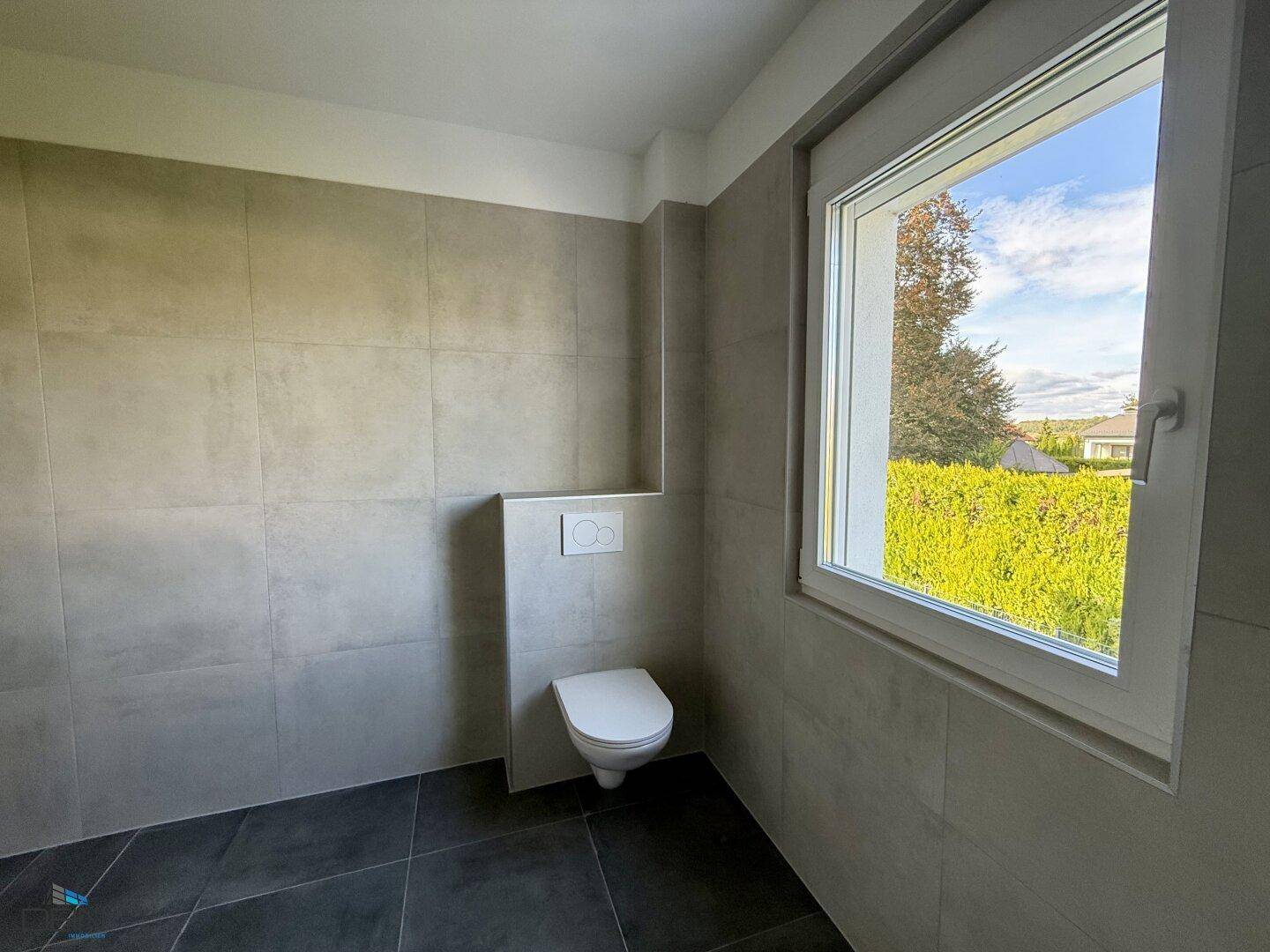 Helles WC mit Wand-WC und großem Fenster, das viel Tageslicht hereinlässt und eine angenehme Atmosphäre schafft.