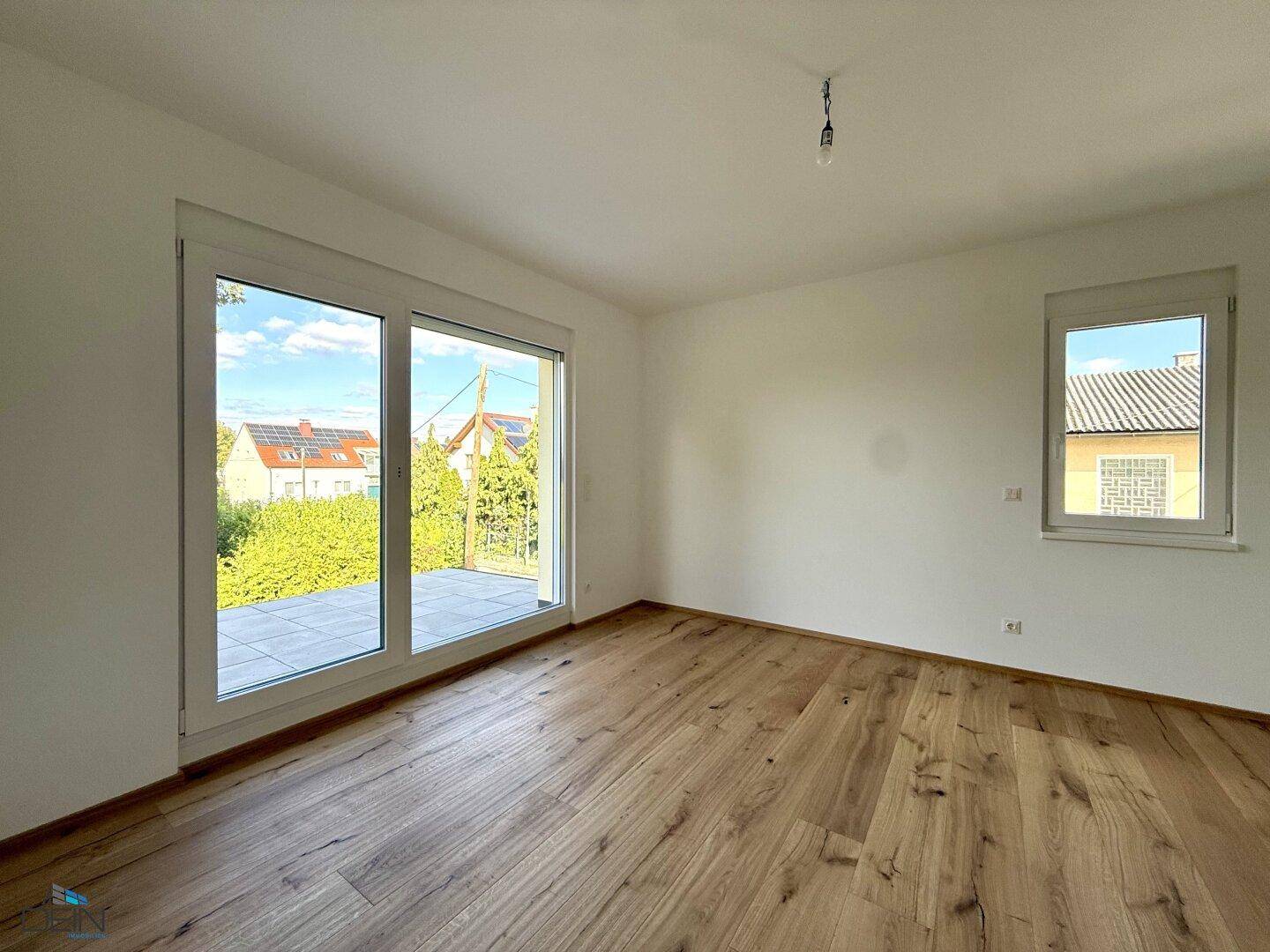 Geräumiges Schlafzimmer mit Holzboden und großem Fenster mit Blick ins Grüne, ideal zum Entspannen.
