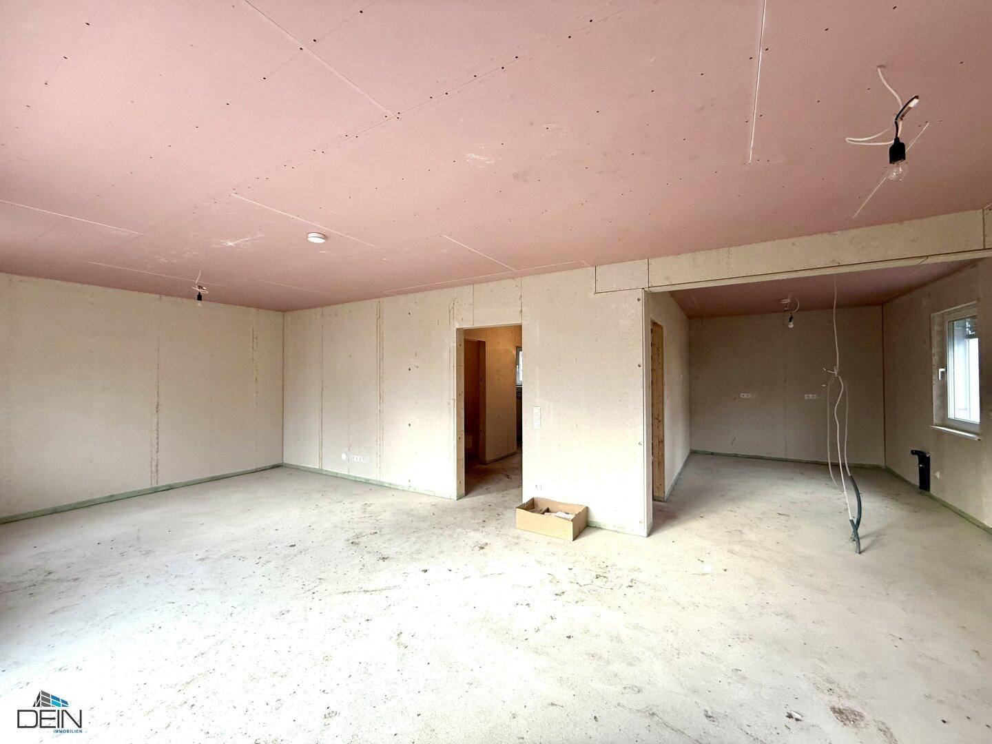 Unfertiger Wohnbereich im Neubau mit rosa Deckenplatten und Rohbauwänden, bereit für den Ausbau.