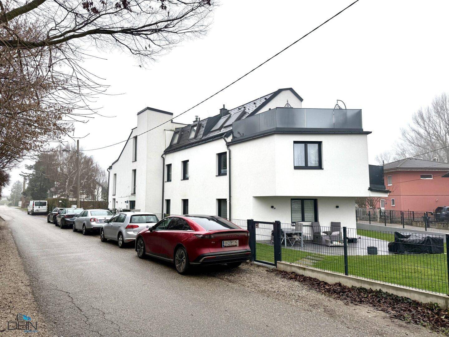 Seitenansicht eines modernen Wohngebäudes mit Parkplätzen entlang der Straße.