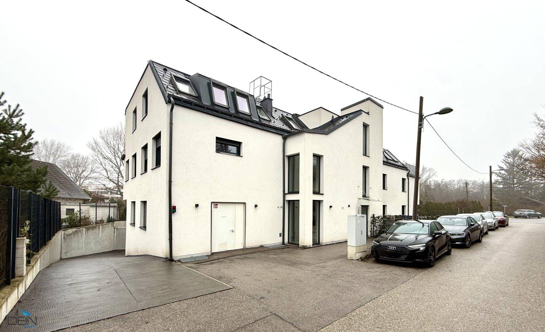 Rückansicht des modernen Wohngebäudes mit Zufahrt zur Tiefgarage und Parkplätzen.
