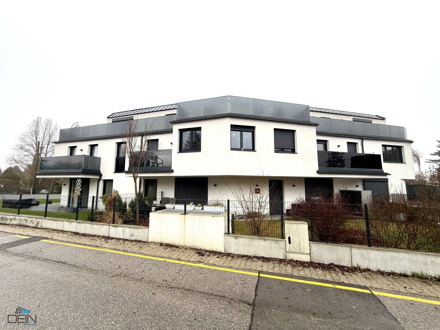 Modernes Mehrfamilienhaus mit weißer Fassade und dunklen Akzenten in winterlicher Umgebung.
