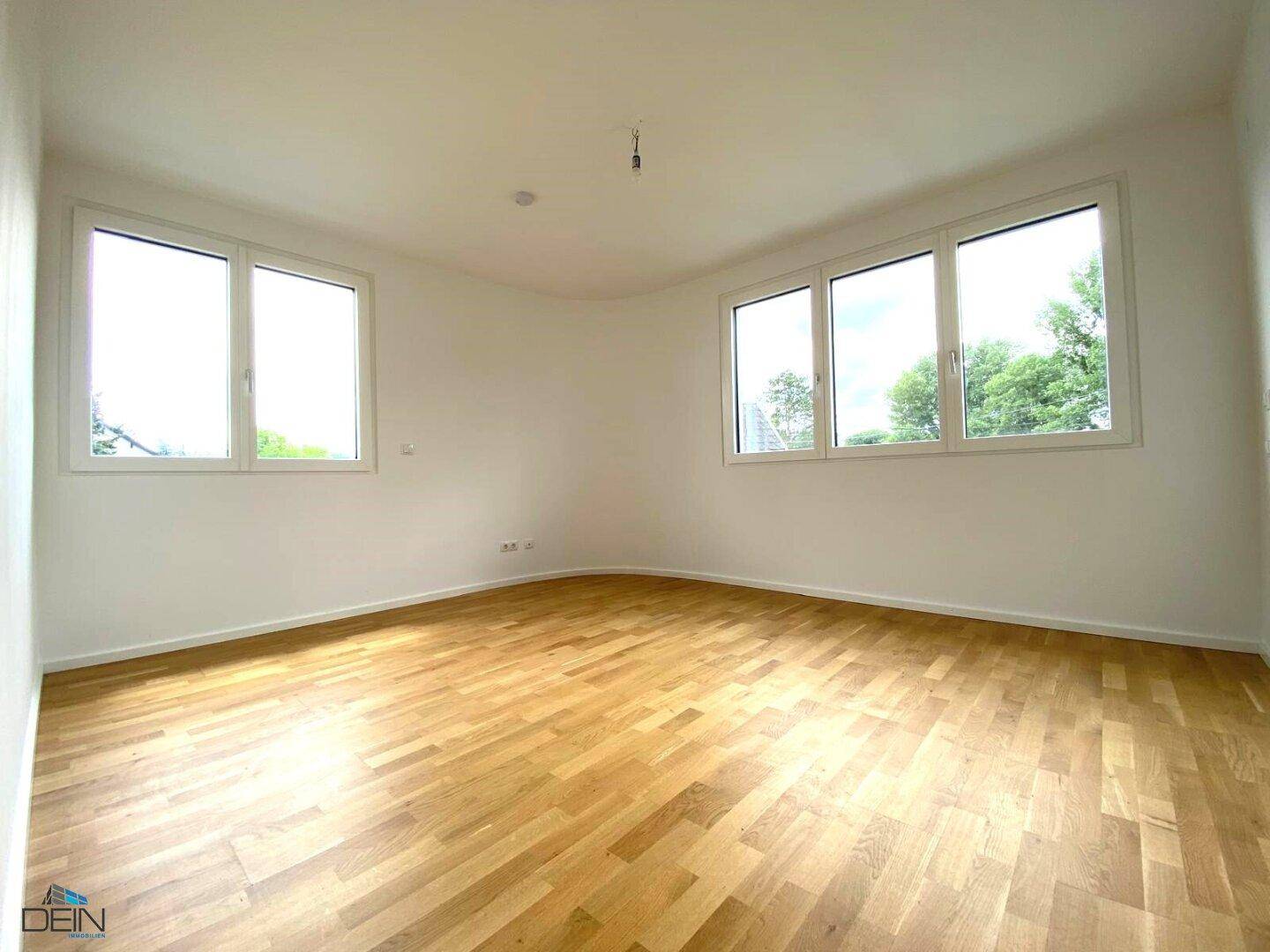 Helles Schlafzimmer mit Holzboden und zwei großen Fenstern, die viel Tageslicht hereinlassen.