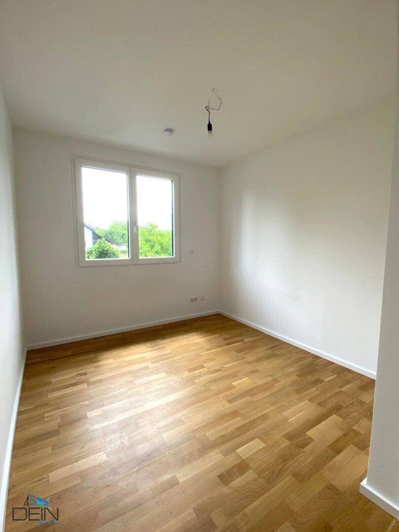 Gemütliches Zimmer mit Holzboden und einem großen Fenster, das einen Blick ins Grüne bietet.