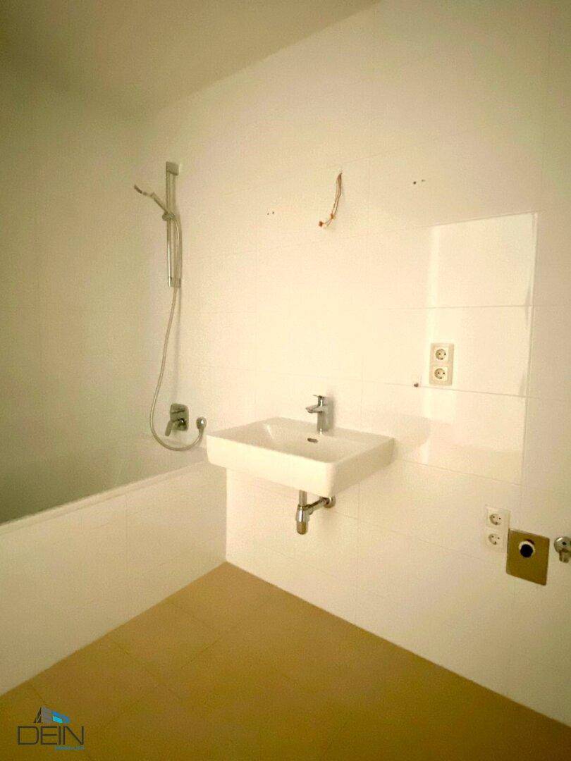 Modernes Badezimmer mit weiß gefliesten Wänden, Waschbecken und Badewanne mit Duschfunktion.