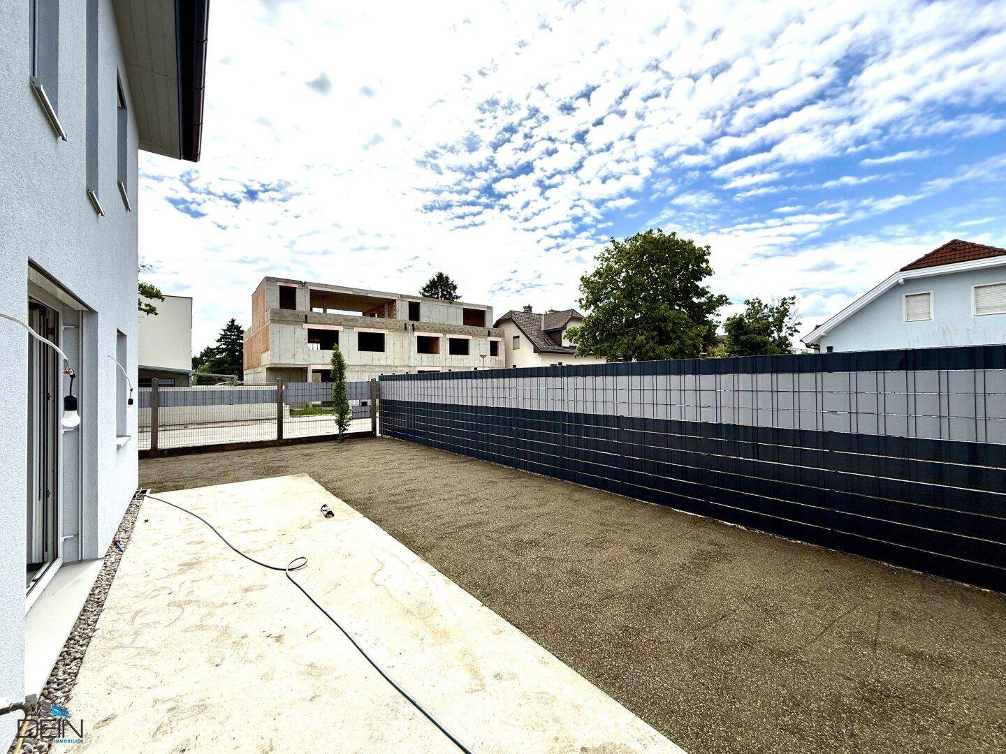 Seitenansicht des Neubaus mit vorbereitetem Gartenbereich und Blick auf die Umgebung.