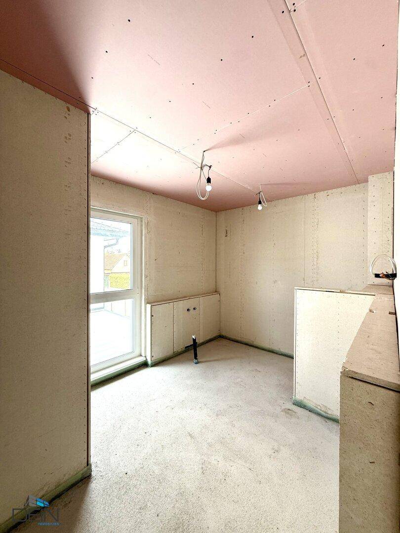Rohbau-Badezimmer mit vorbereiteten Anschlüssen für Sanitäranlagen und einem Fenster.