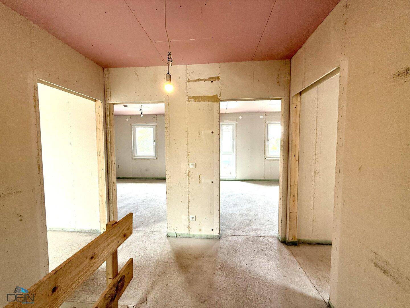 Unfertiger Flurbereich im Neubau mit mehreren Türöffnungen und rosa Deckenplatten.