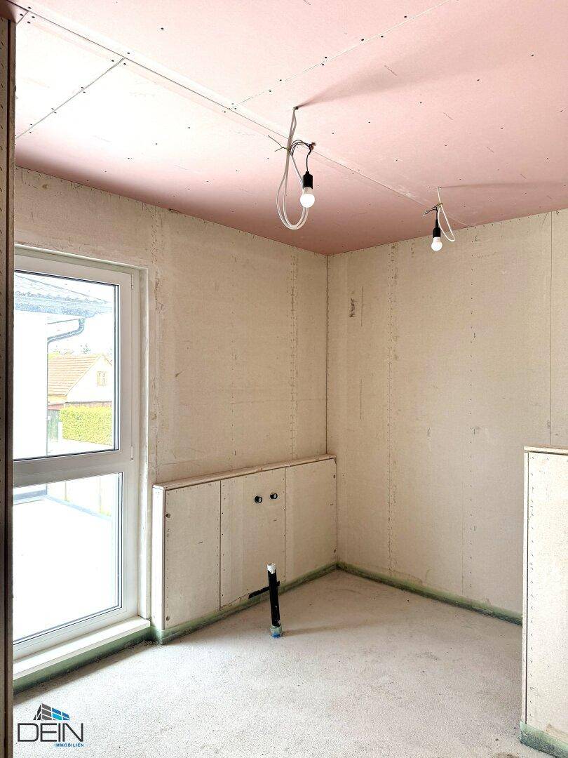 Rohbau-Badezimmer mit vorbereiteten Anschlüssen für Sanitäranlagen und einem Fenster.