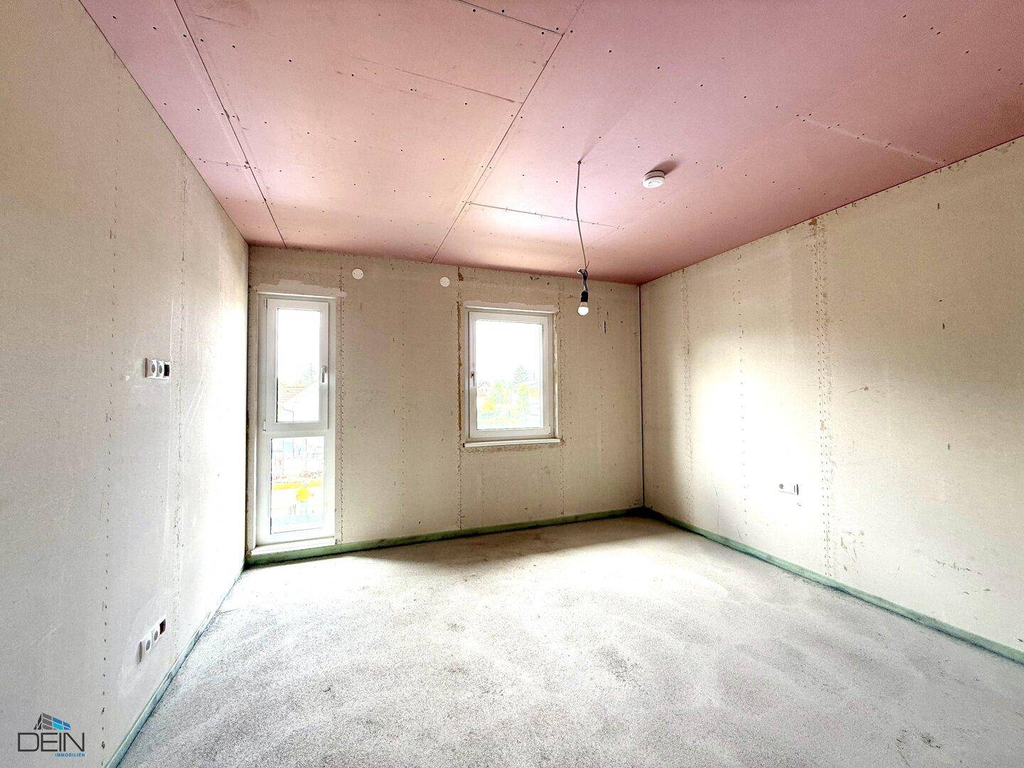 Unfertiges Schlafzimmer im Neubau mit zwei Fenstern und rosa Deckenplatten, bereit für den Ausbau.