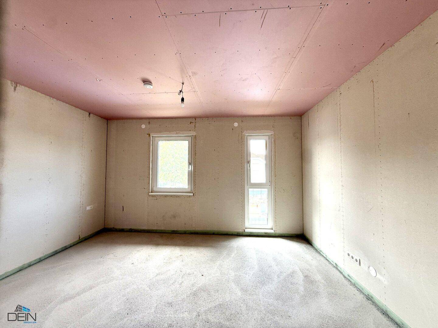 Unfertiges Schlafzimmer im Neubau mit zwei Fenstern und rosa Deckenplatten, bereit für den Ausbau.