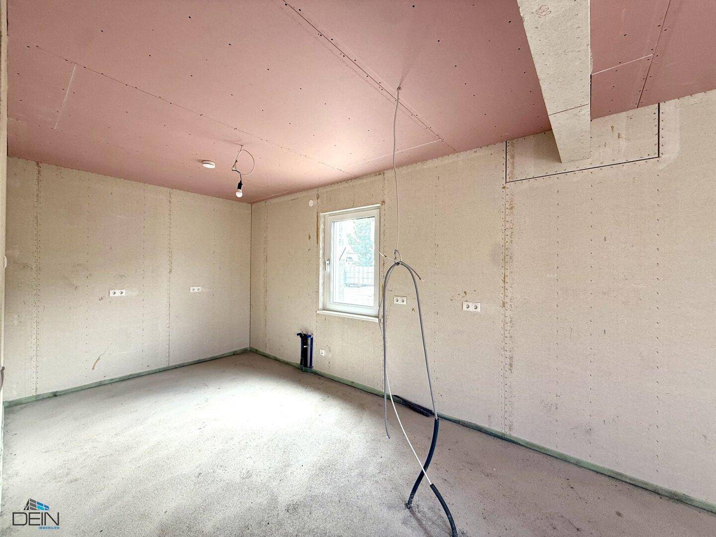 Unfertiger Raum im Neubau mit Fenster und rosa Deckenplatten, bereit für die weitere Gestaltung.