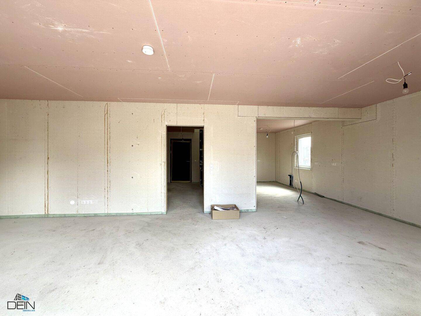 Geräumiger Rohbau-Wohnbereich mit rosa Deckenplatten und vorbereiteten Wänden für den Innenausbau.