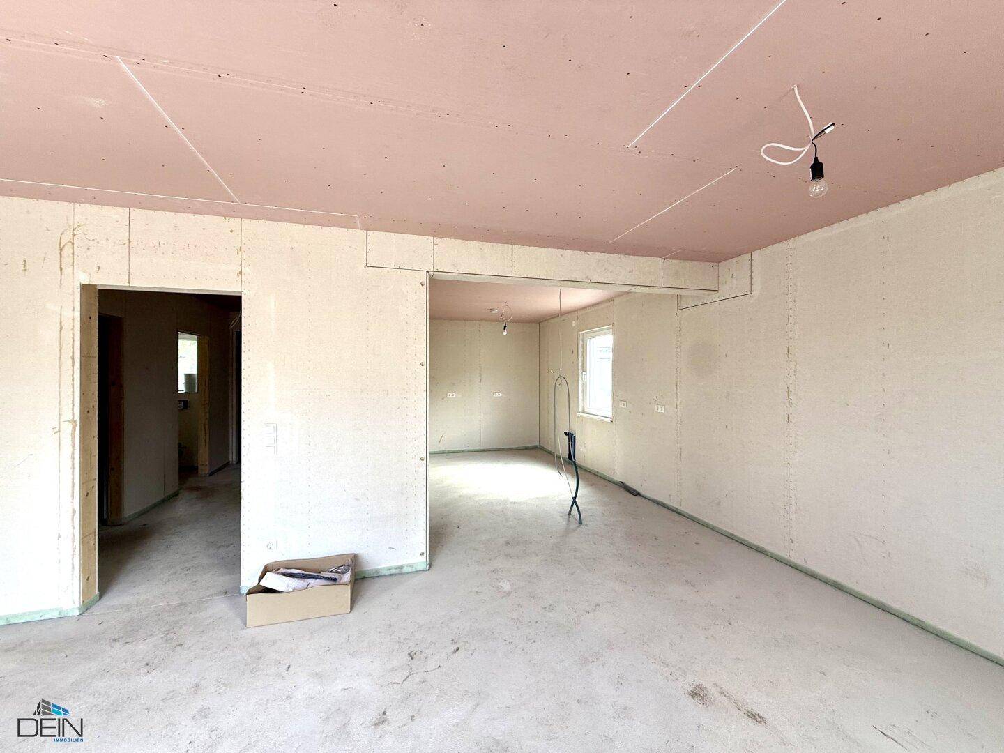 Rohbau-Wohnbereich mit Blick auf den Fensterbereich und rosa Deckenplatten, wartet auf Fertigstellung.