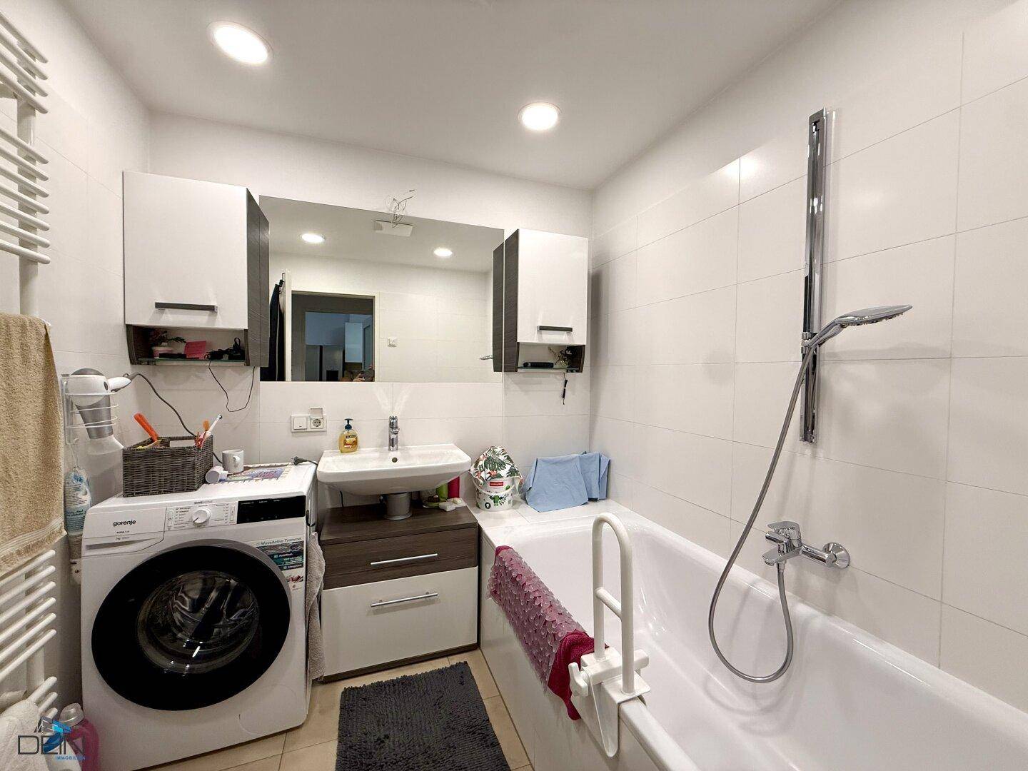 Badezimmer mit Badewanne, Waschmaschine, Waschbecken und Wandspiegel.