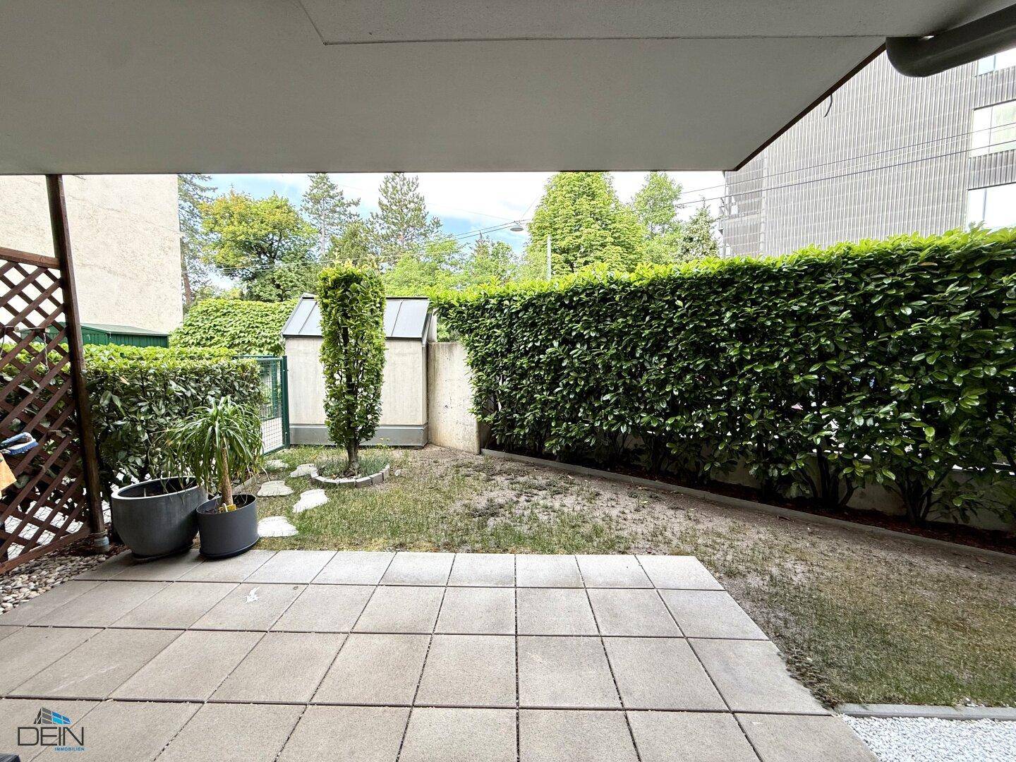 Gepflegter Gartenbereich mit Hecke und kleinen Gartenhäuschen im Hintergrund.