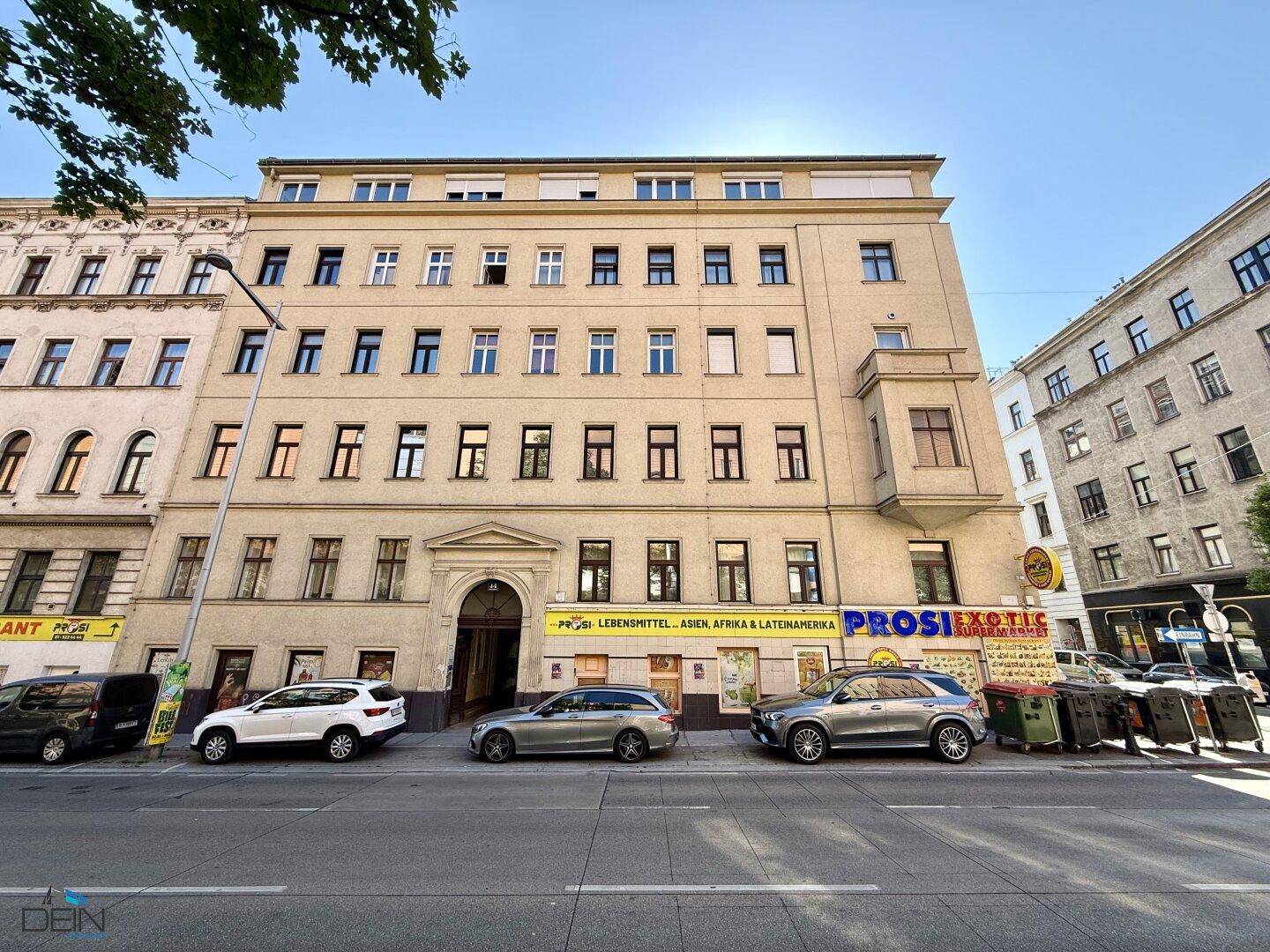 Klassische Fassade eines Mehrfamilienhauses an einer städtischen Straße mit parkenden Autos.