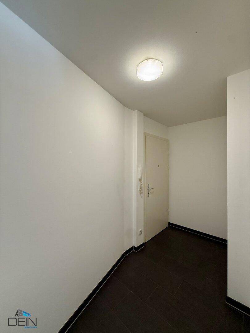 Schlichter Flur mit dunklen Fliesen und weißen Wänden, der zu einer hellen Zimmertür führt.
