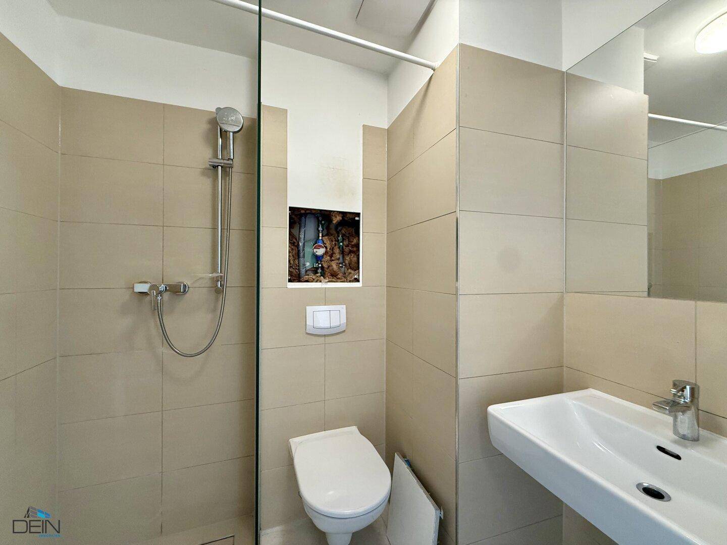Modernes Badezimmer mit beigefarbenen Fliesen, Duschbereich, WC und einem Waschbecken mit großem Spiegel.
