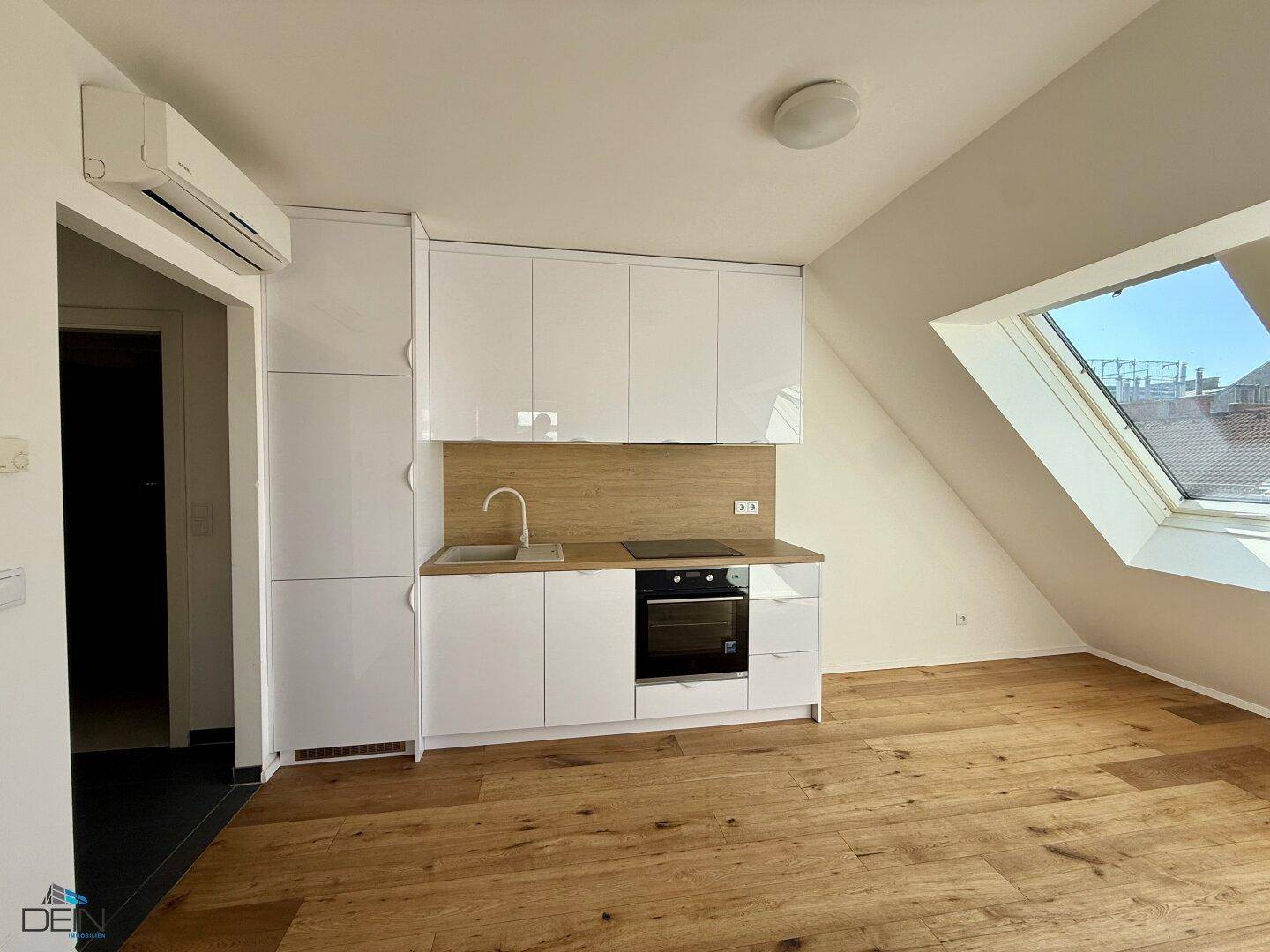 Funktionale Küchenzeile mit weißen Schränken und Klimaanlage in einem hellen Raum mit Holzboden.