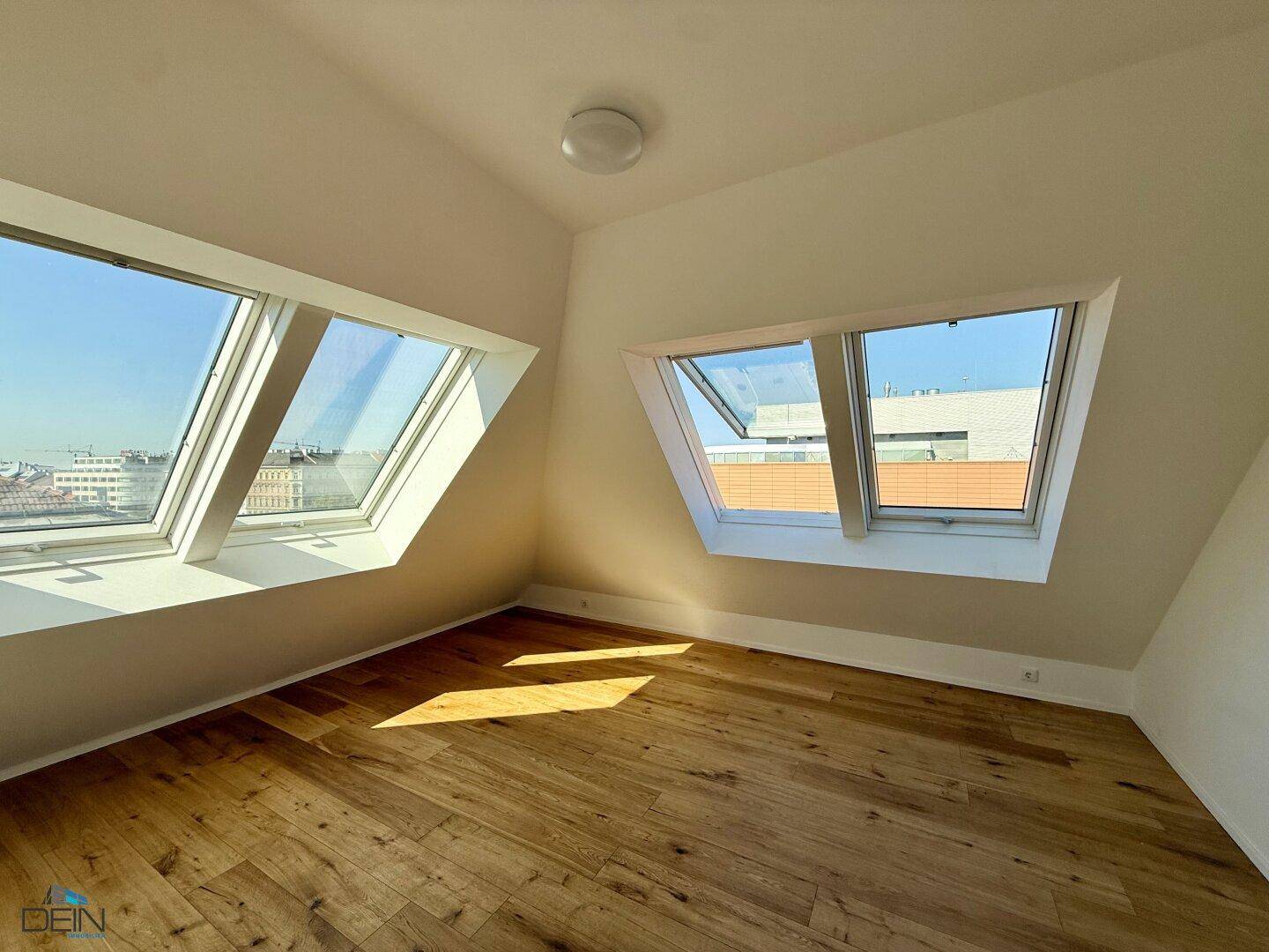 Geräumiger, heller Raum mit Holzboden, Dachschrägen und zwei großen Dachfenstern für viel Tageslicht.