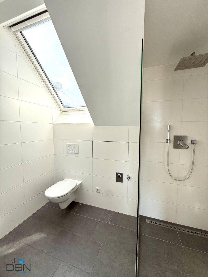 Modernes Badezimmer mit begehbarer Dusche, Wand-WC und Dachfenster für Belüftung.