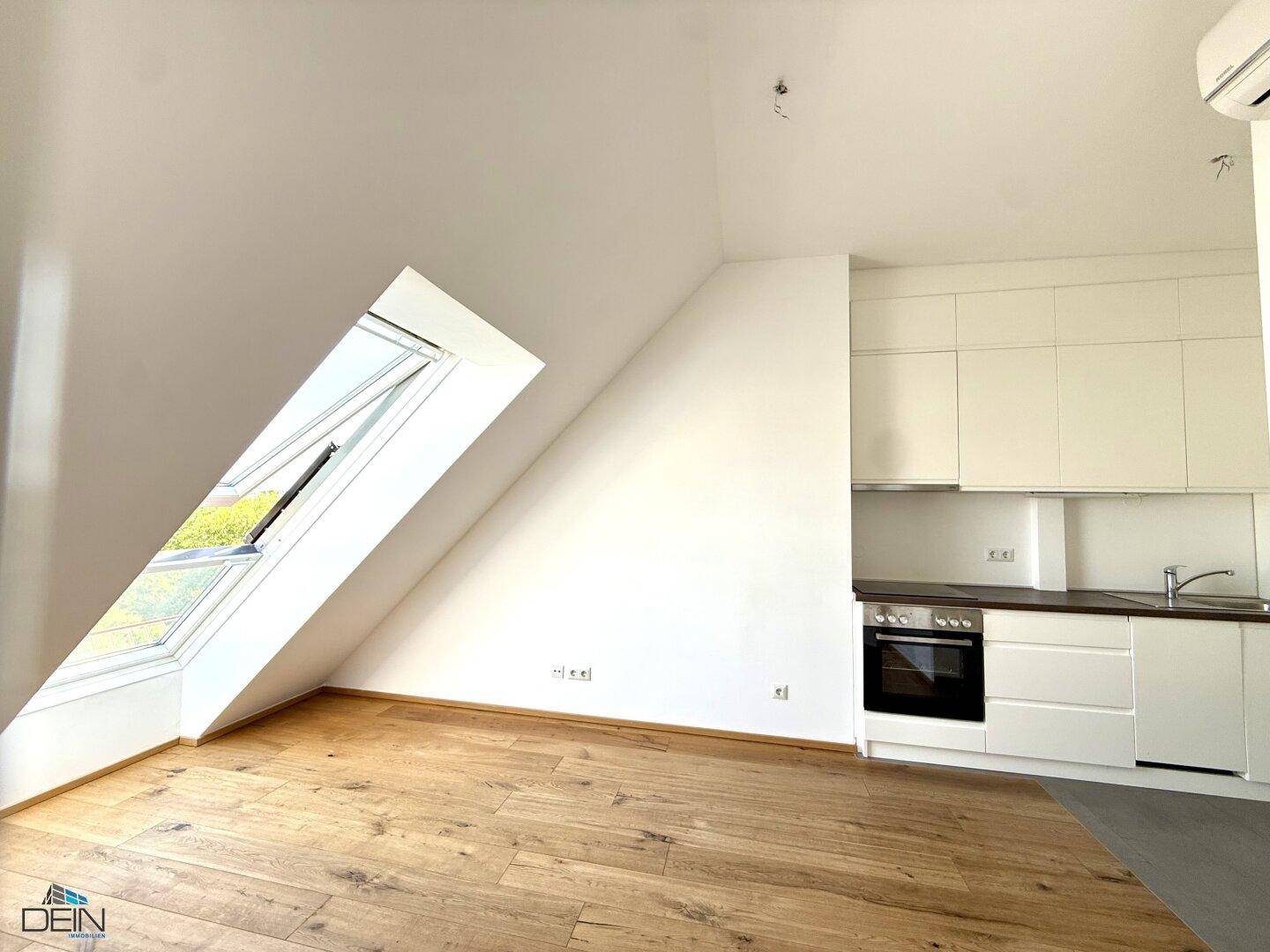 Offener Wohnbereich mit integrierter Küchenzeile und großem Dachfenster, das den Raum erhellt.