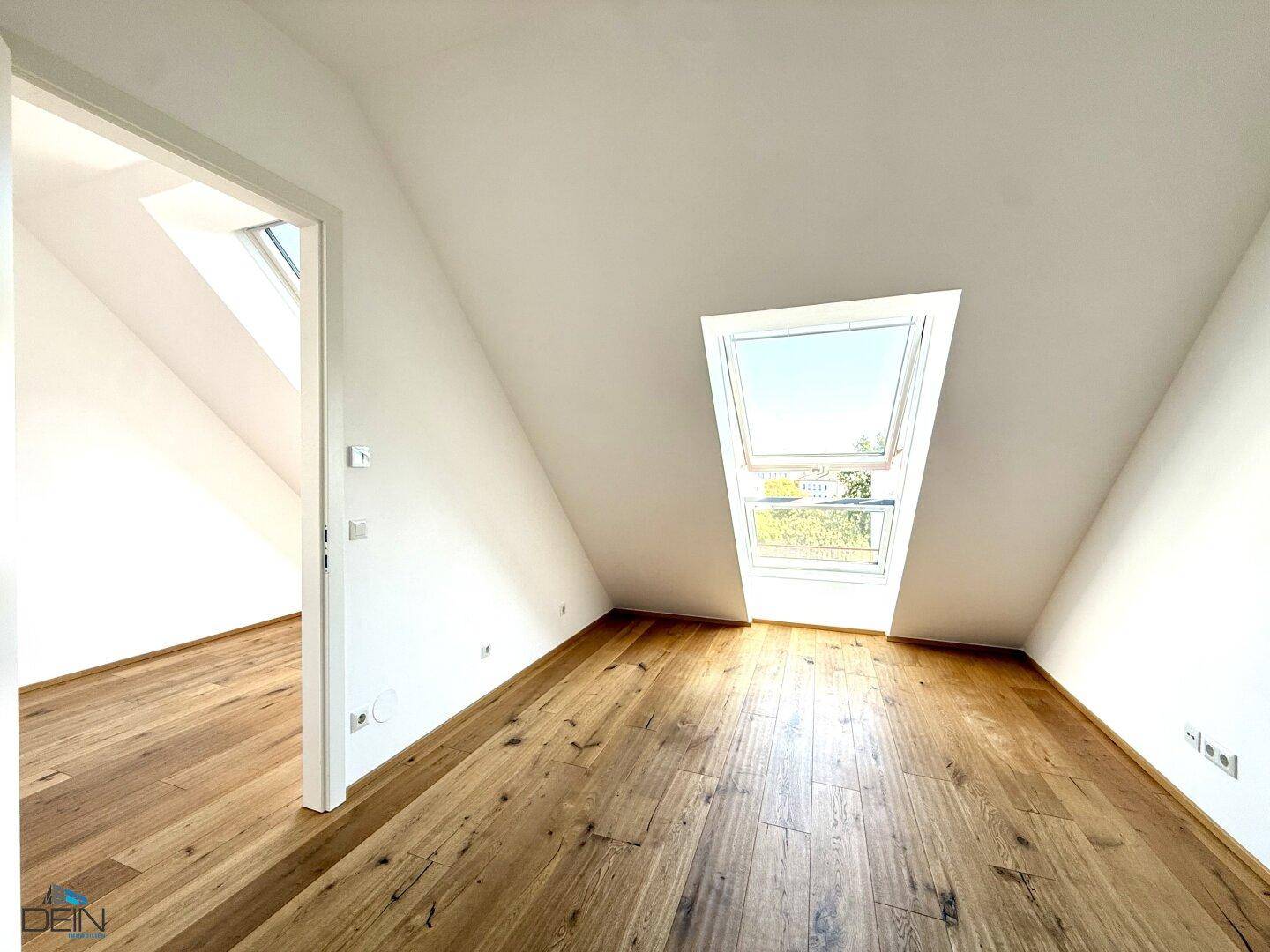 Helles Zimmer im Dachgeschoss mit Holzboden und einem großen Dachfenster, das viel Licht spendet.