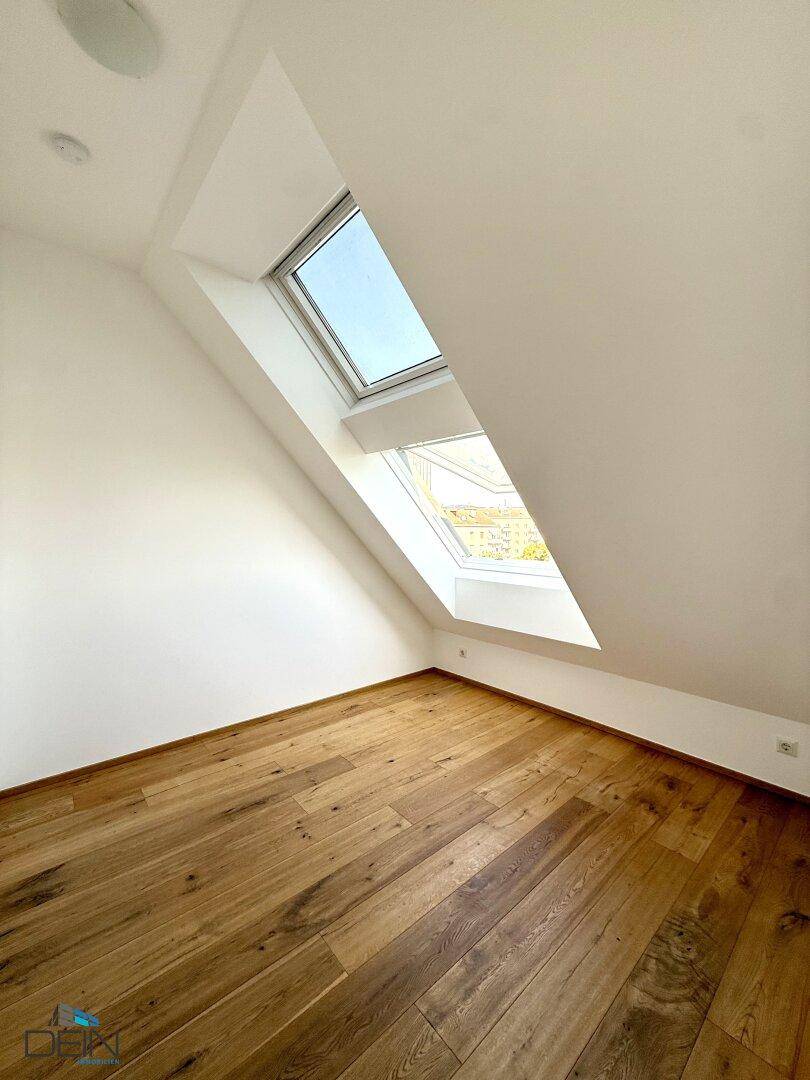 Lichtdurchflutetes Zimmer mit Holzboden und schrägen Wänden, ausgestattet mit einem Dachfenster.