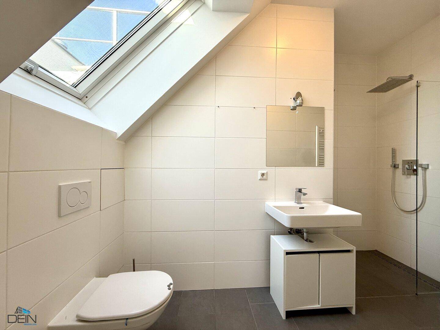 Modernes Badezimmer mit weißen Fliesen, Dusche und Dachfenster für natürliches Licht.