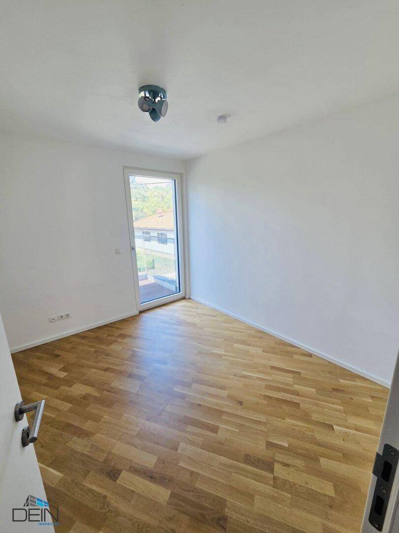 Helles Zimmer mit Parkettboden und Zugang zu einem Balkon oder einer Terrasse.