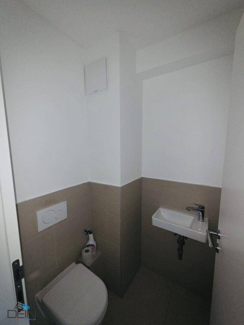 Modernes Gäste-WC mit Wand-WC, kleinem Waschbecken und beigefarbenen Fliesen.