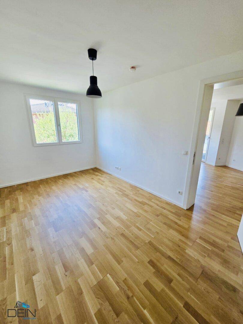 Helles Zimmer mit Parkettboden, weiß gestrichenen Wänden und Blick ins Grüne.