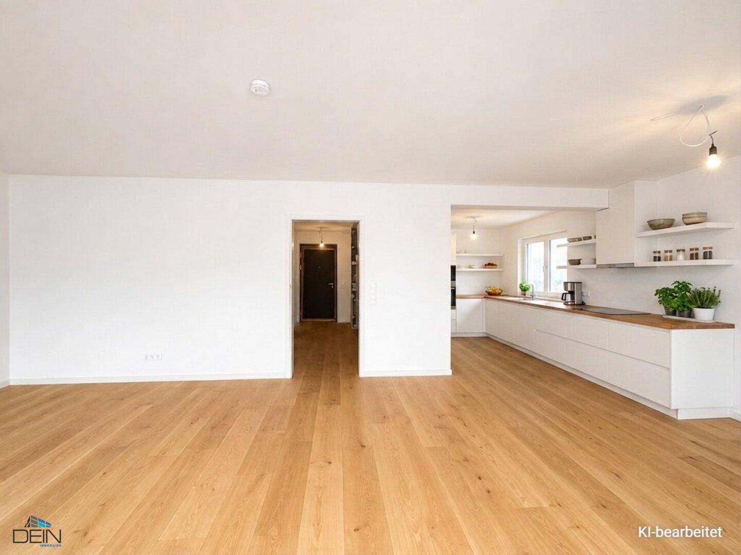 Heller offener Wohnbereich mit Holzboden und moderner weißer Einbauküche mit Holztheke.