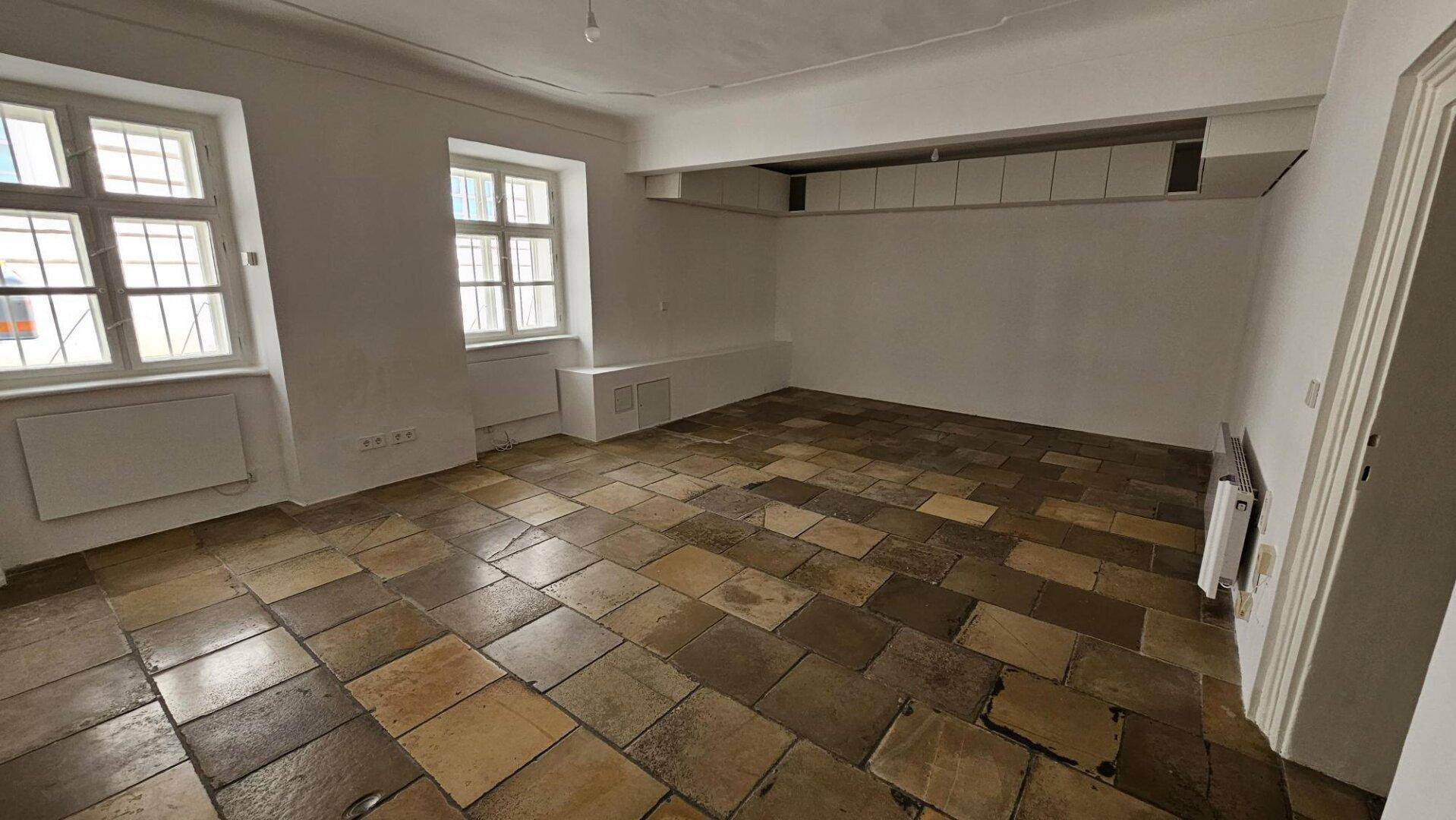 Geräumiger, leerer Raum mit charakteristischem Steinboden und hellen Wänden, ideal für individuelle Gestaltung.