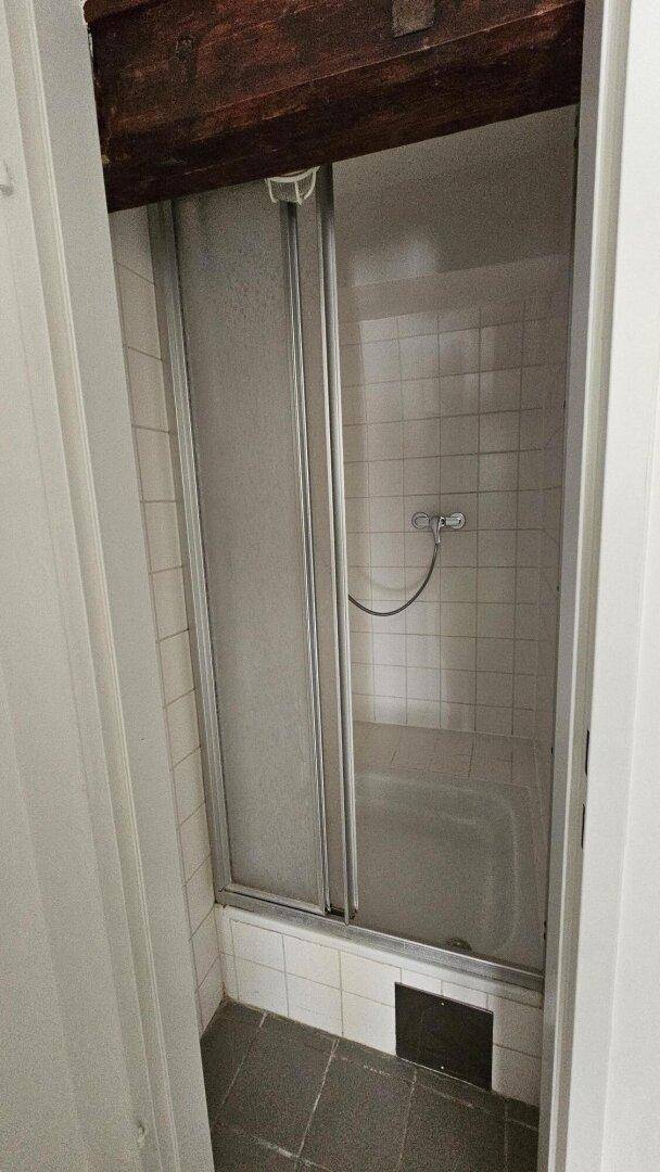 Duschkabine mit Schiebetüren und weißen Fliesen, integriert in ein kleines Badezimmer.